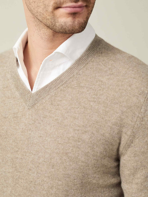 Close-up detail of a man wearing a camel beige cashmere V-neck sweater over a white shirt, showcasing the ribbed neckline.