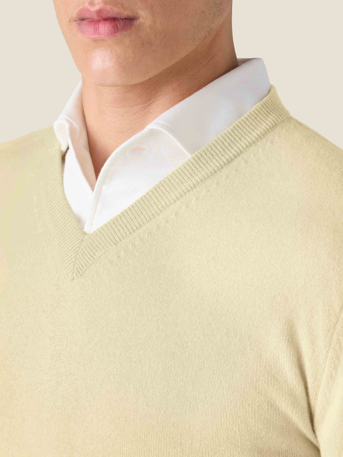 Model wears a yellow pure cashmere V-neck jumper over a white shirt in a close-up shot highlighting the ribbed neckline.