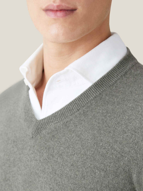 Close-up of the moss green cashmere V-neck jumper, showing the ribbed neckline detail layered over a white shirt.