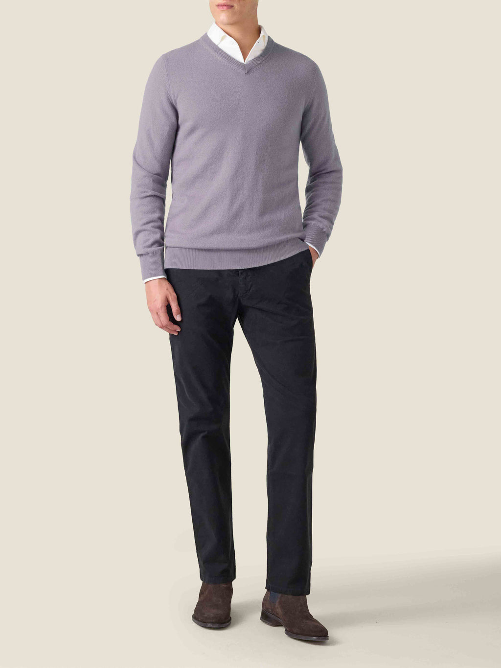 A man wears the violet cashmere V-neck sweater layered over a white shirt, paired with dark trousers and brown boots.