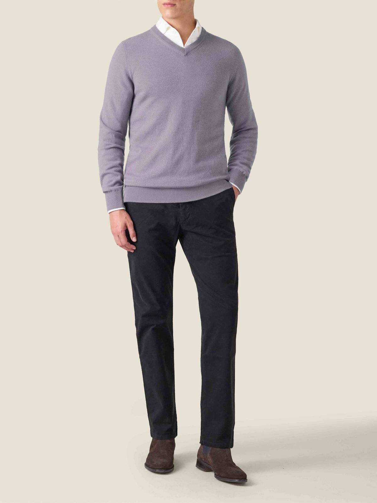 A man wears the violet cashmere V-neck sweater layered over a white shirt, paired with dark trousers and brown boots.