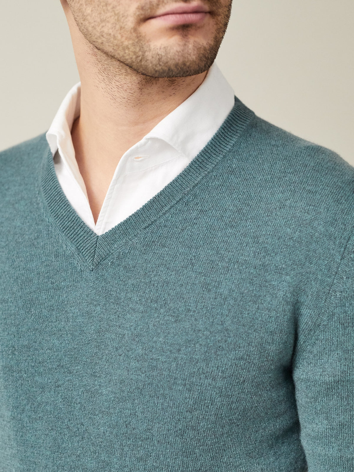 Close-up of a man wearing a marine green cashmere v-neck sweater layered over a white collared shirt.
