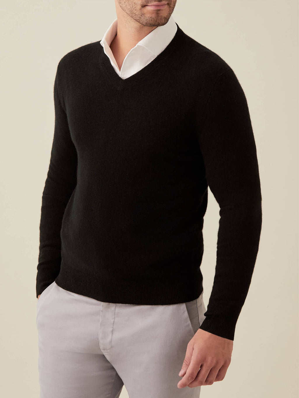 A model wears the Luca Faloni black cashmere V-neck sweater over a white shirt and light grey trousers.