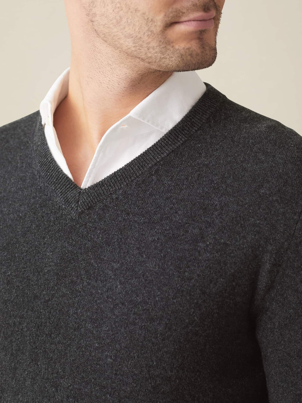 A close-up of a model wearing a charcoal grey cashmere V-neck sweater over a white collared shirt, highlighting the neckline.