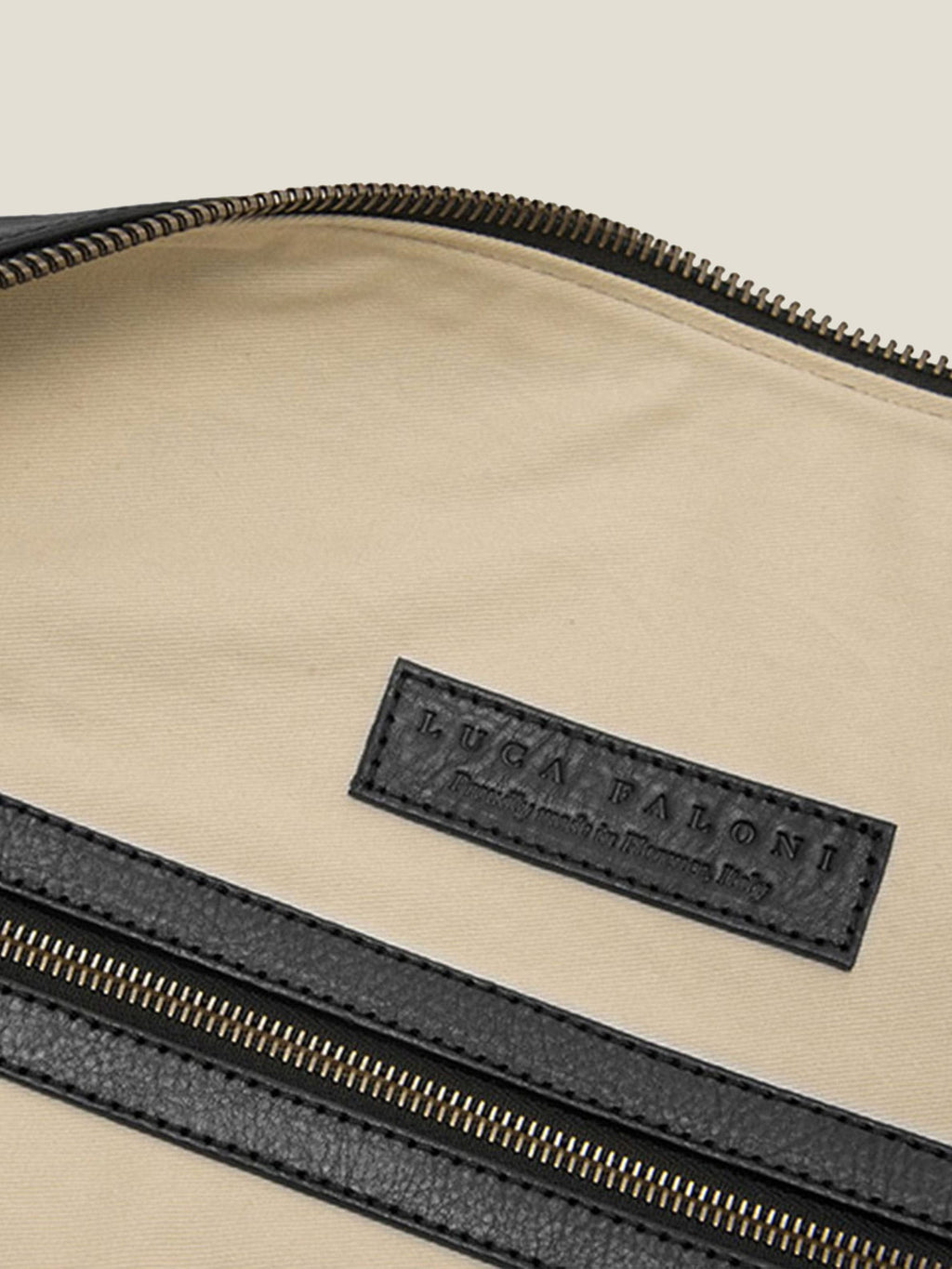 Interior detail of the Luca Faloni black leather Weekender, highlighting the embossed leather brand tag and zipped pocket.
