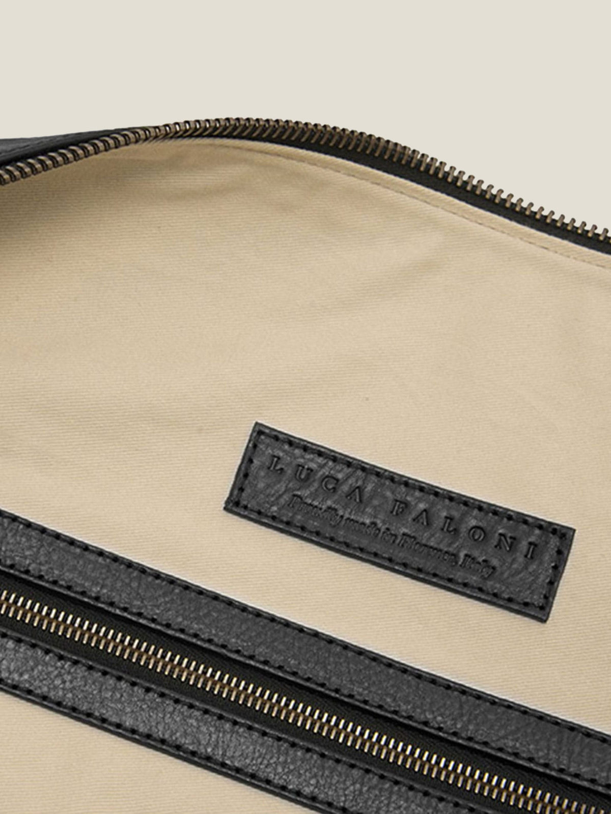 Interior detail of the Luca Faloni black leather Weekender, highlighting the embossed leather brand tag and zipped pocket.