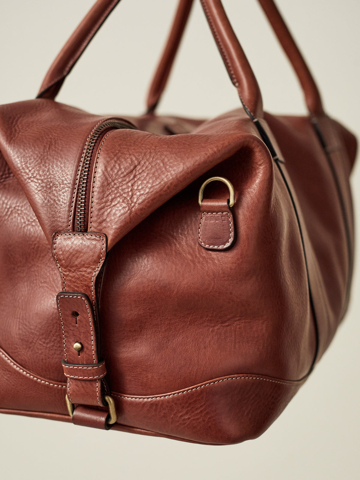 Detail of the Luca Faloni Weekender leather bag in Caramel Brown, showing the side buckle, zipper and full-grain texture.