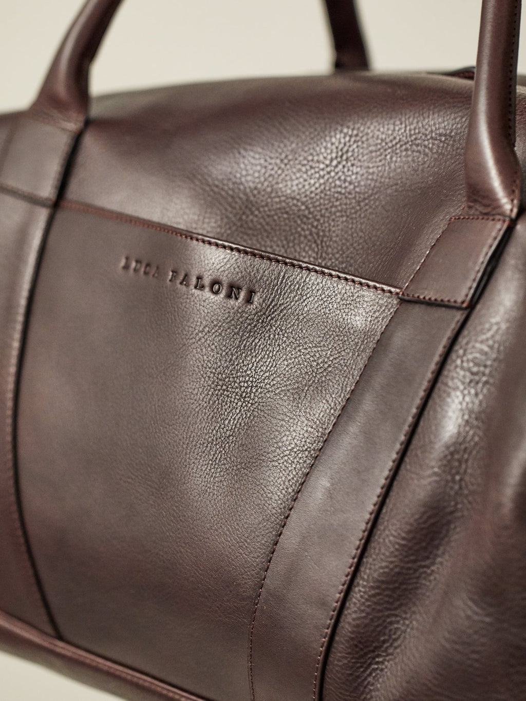 Close-up of the Luca Faloni Weekender in chocolate brown, showing the full-grain leather texture and debossed logo.