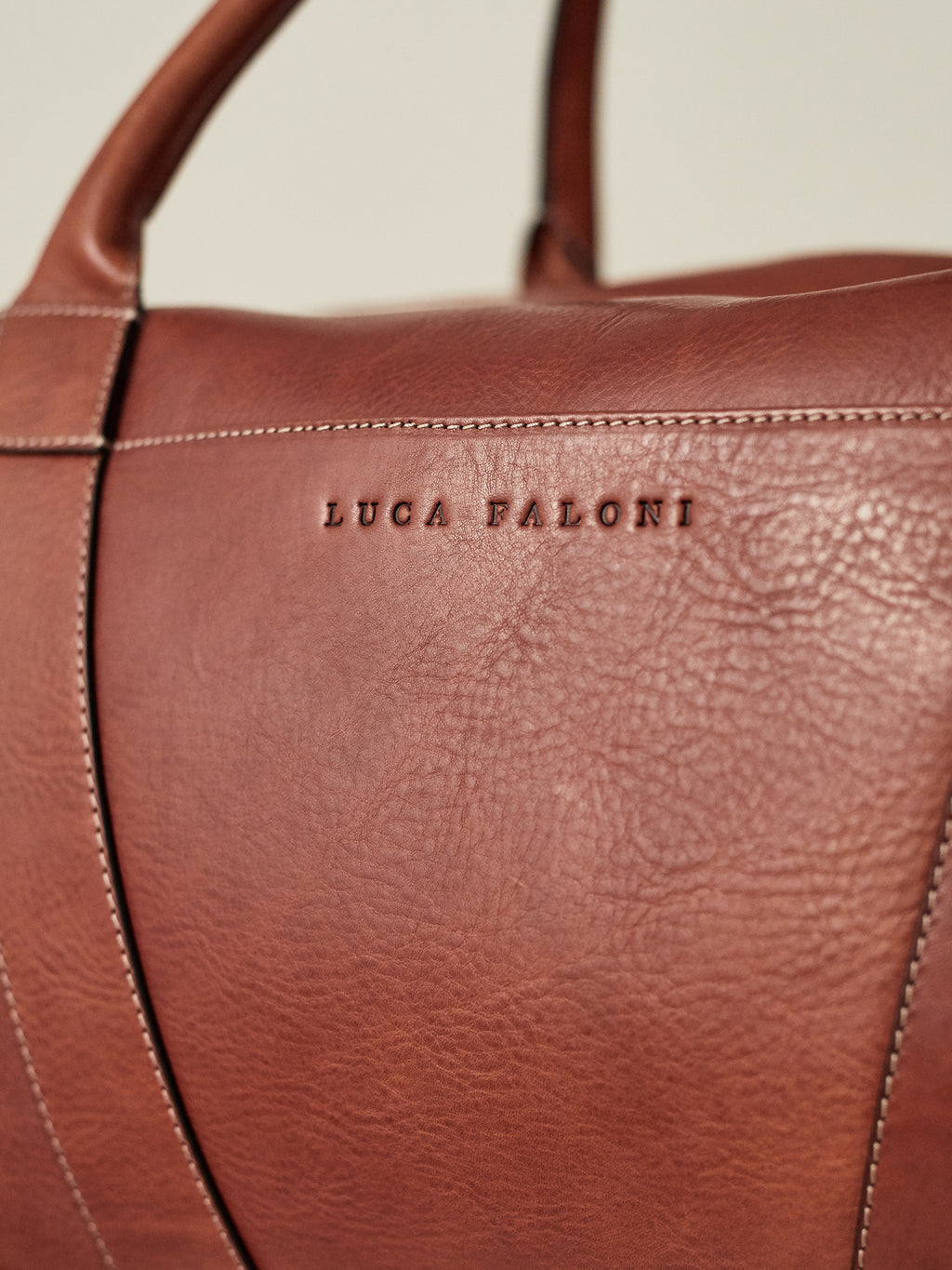 Close-up of the embossed Luca Faloni logo on the full-grain Caramel Brown leather of the Weekender travel bag.