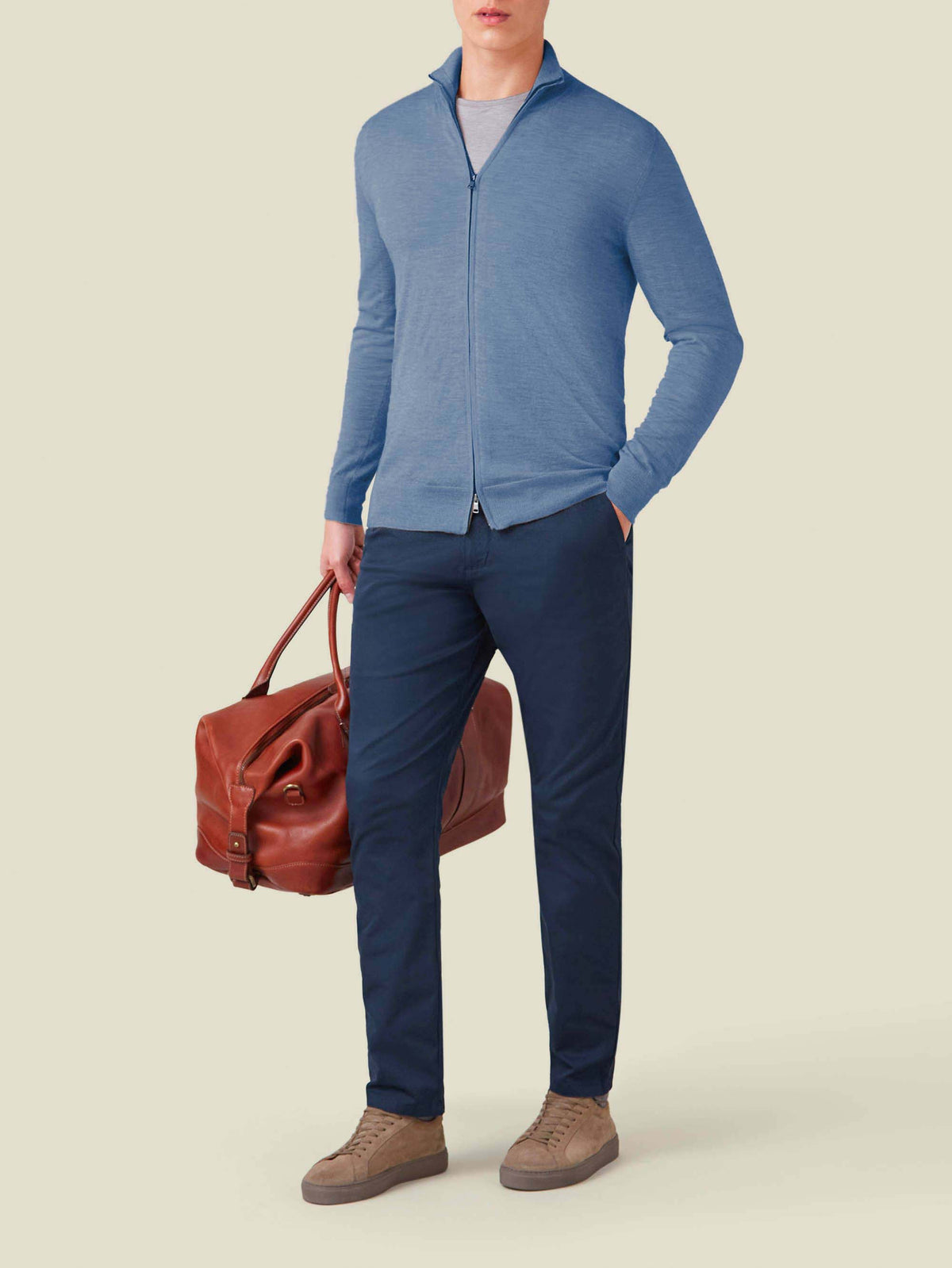 Full view of a model wearing the Azure Silk-Cashmere Zip Cardigan with navy trousers and holding a brown leather holdall.
