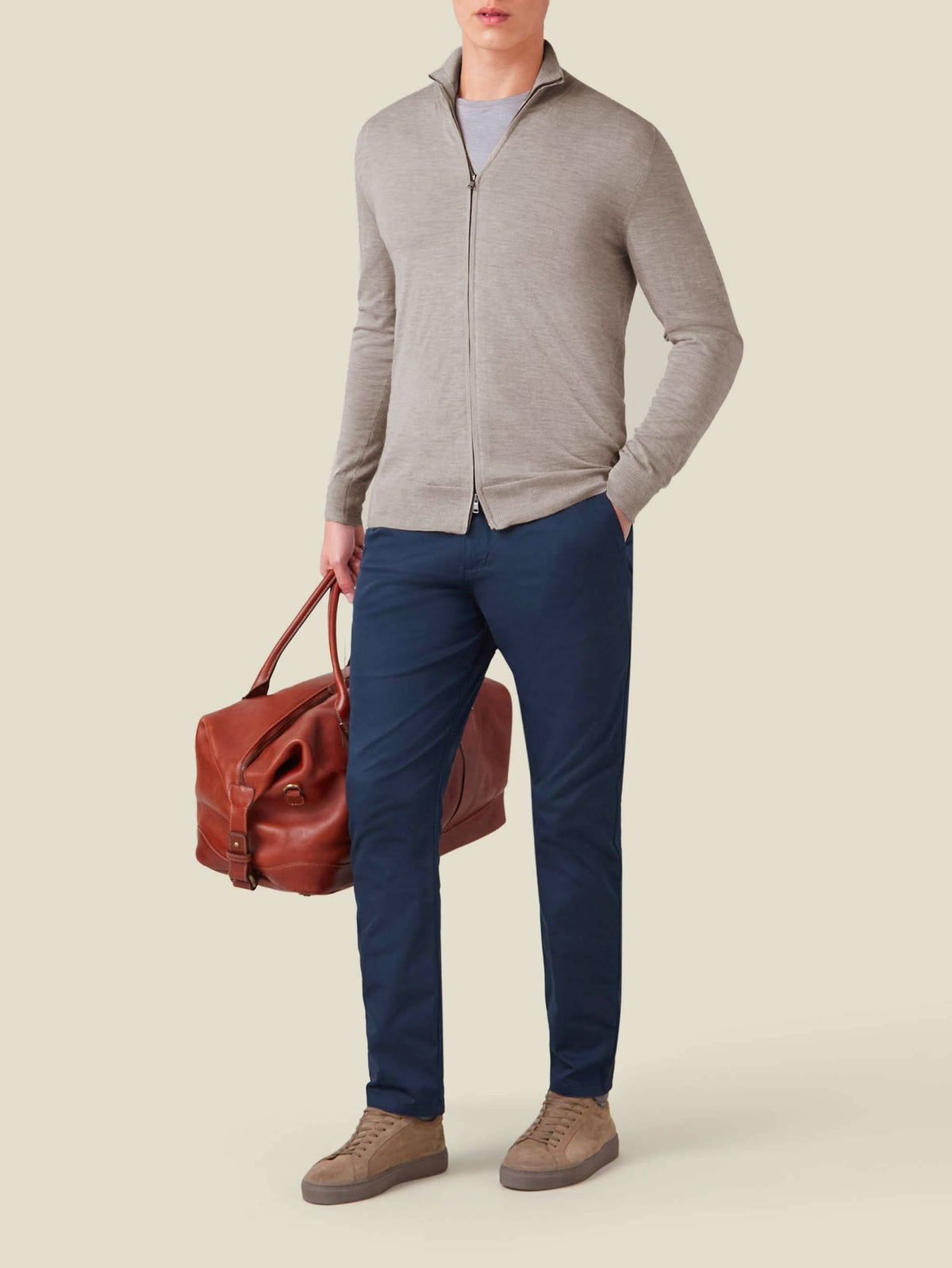A man wears the Nocciola Brown Silk-Cashmere Zip Cardigan with navy trousers and holds a leather duffle bag.
