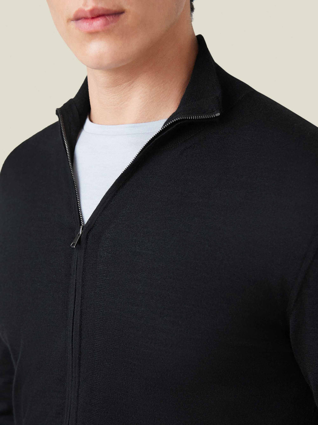 A close-up of a man wearing the black silk-cashmere zip cardigan, showing the fine-knit texture and funnel collar detail.