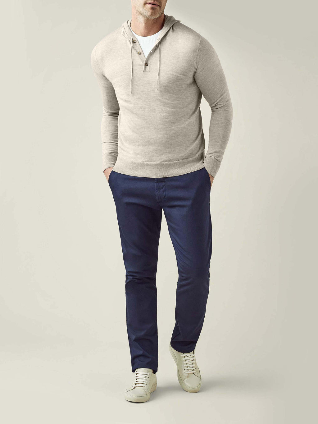 A model wears the Luca Faloni Silk-Cashmere Hoodie in Oatmeal, styled with dark navy trousers and white sneakers.