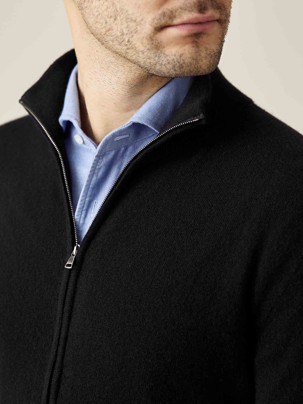 A close-up of a man wearing Luca Faloni's black cashmere zip cardigan, detailing the funnel collar and zipper.