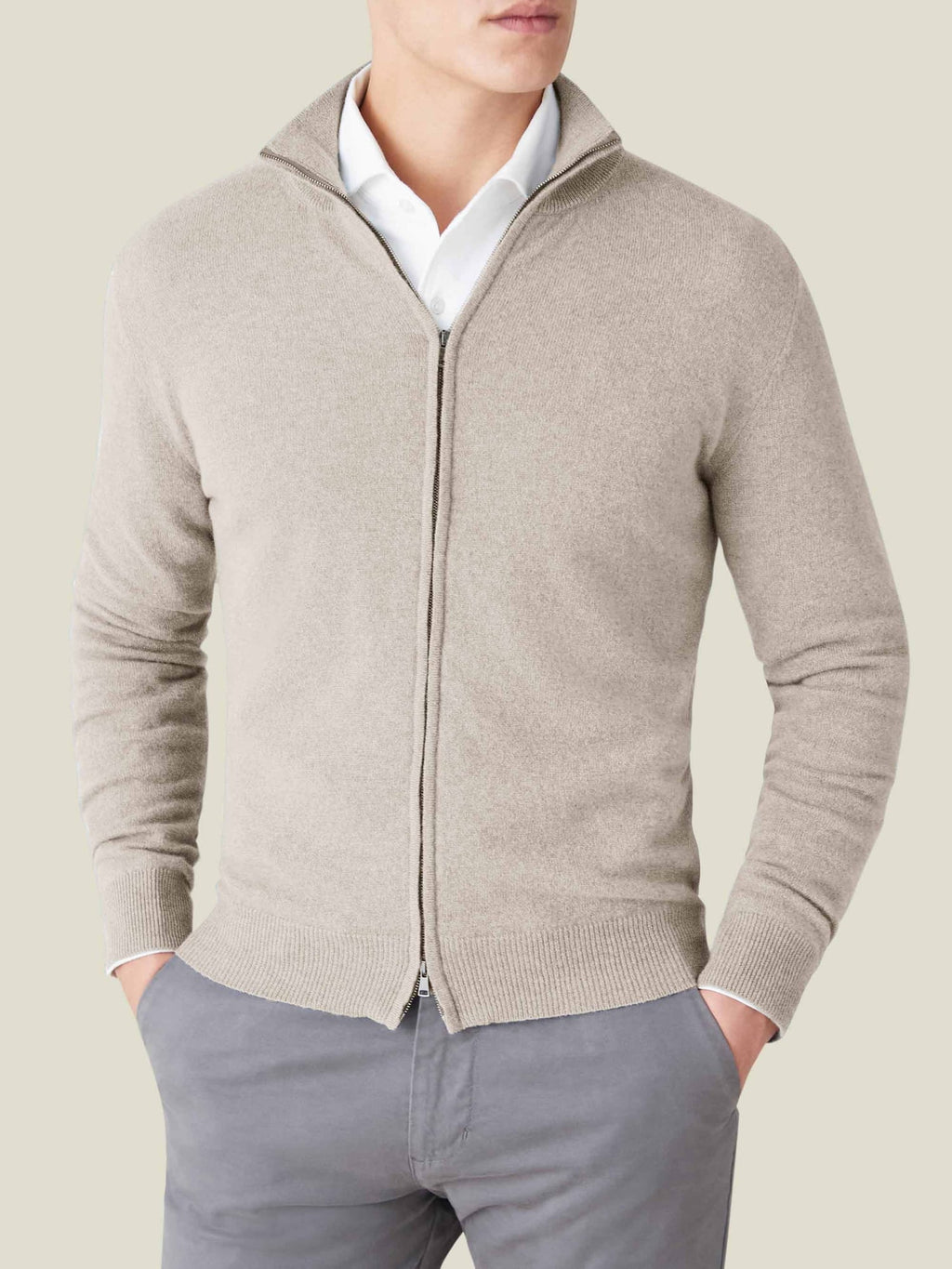 Model wears the Luca Faloni almond cashmere zip cardigan, layered over a white shirt and paired with grey trousers.