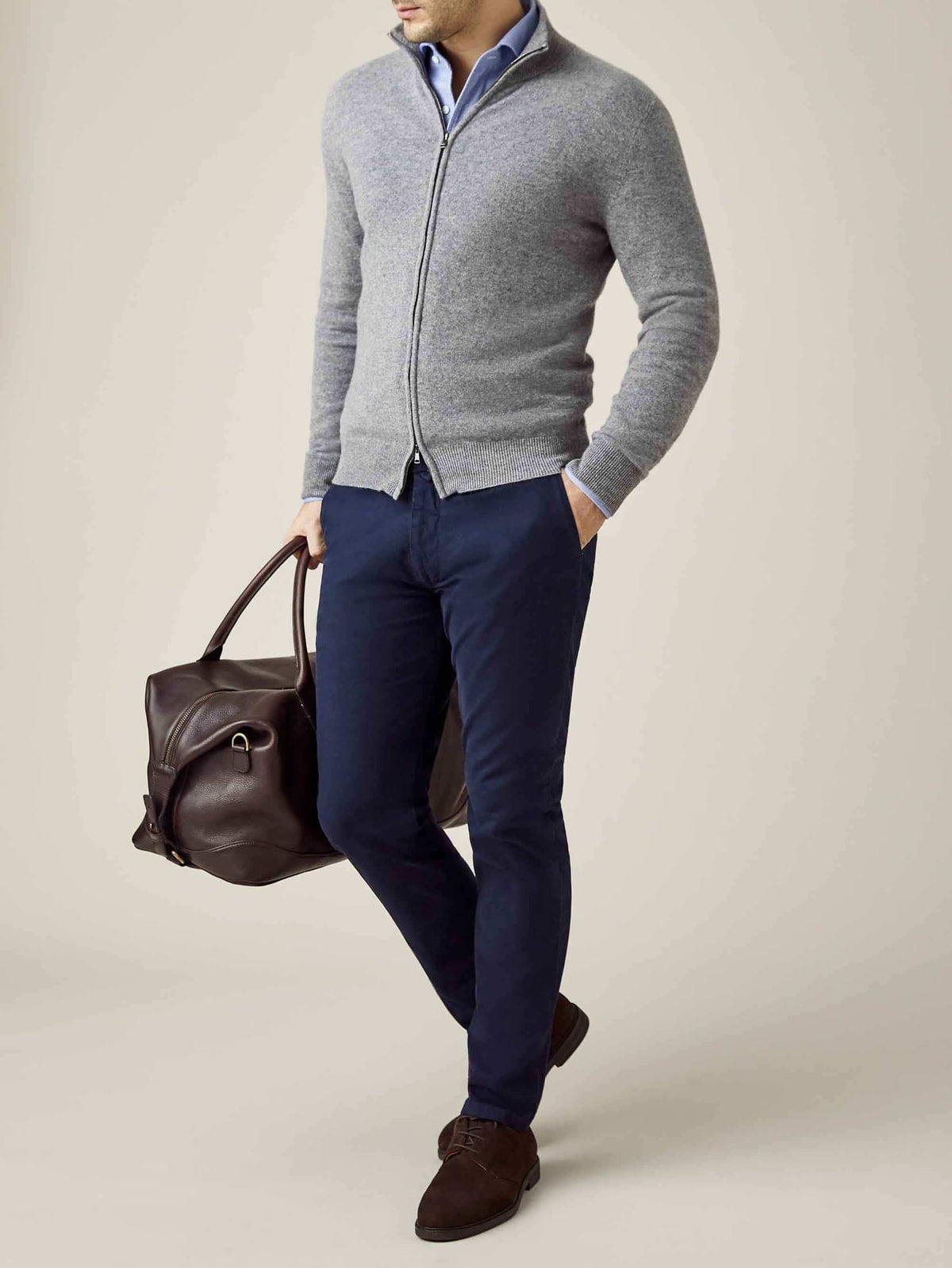 Man wearing the Luca Faloni Dolomiti Grey Cashmere Zip Cardigan with navy trousers and carrying a brown leather holdall bag.