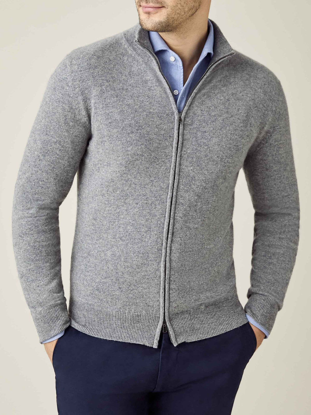 Model wears the Luca Faloni cashmere zip cardigan in Dolomiti grey, styled over a blue shirt and navy trousers.