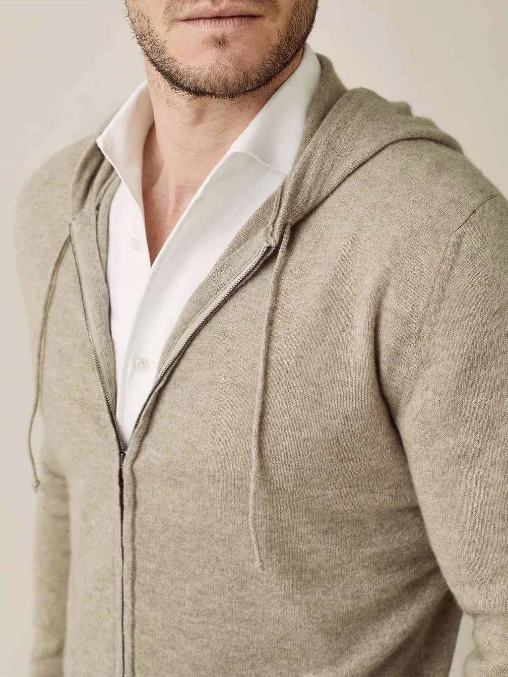 Detail shot of a man wearing the camel beige cashmere zip hoodie, styled open over a white collared shirt.