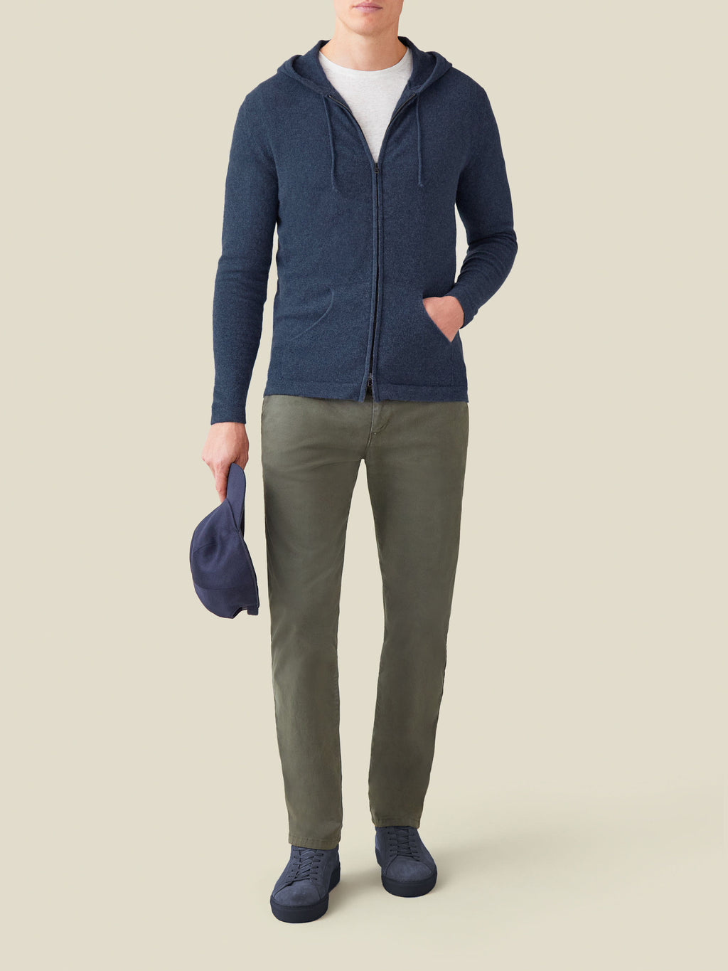 Model wears the Atlantic Blue Cashmere Zip Hoodie with a white t-shirt, olive trousers and blue sneakers, holding a blue cap.
