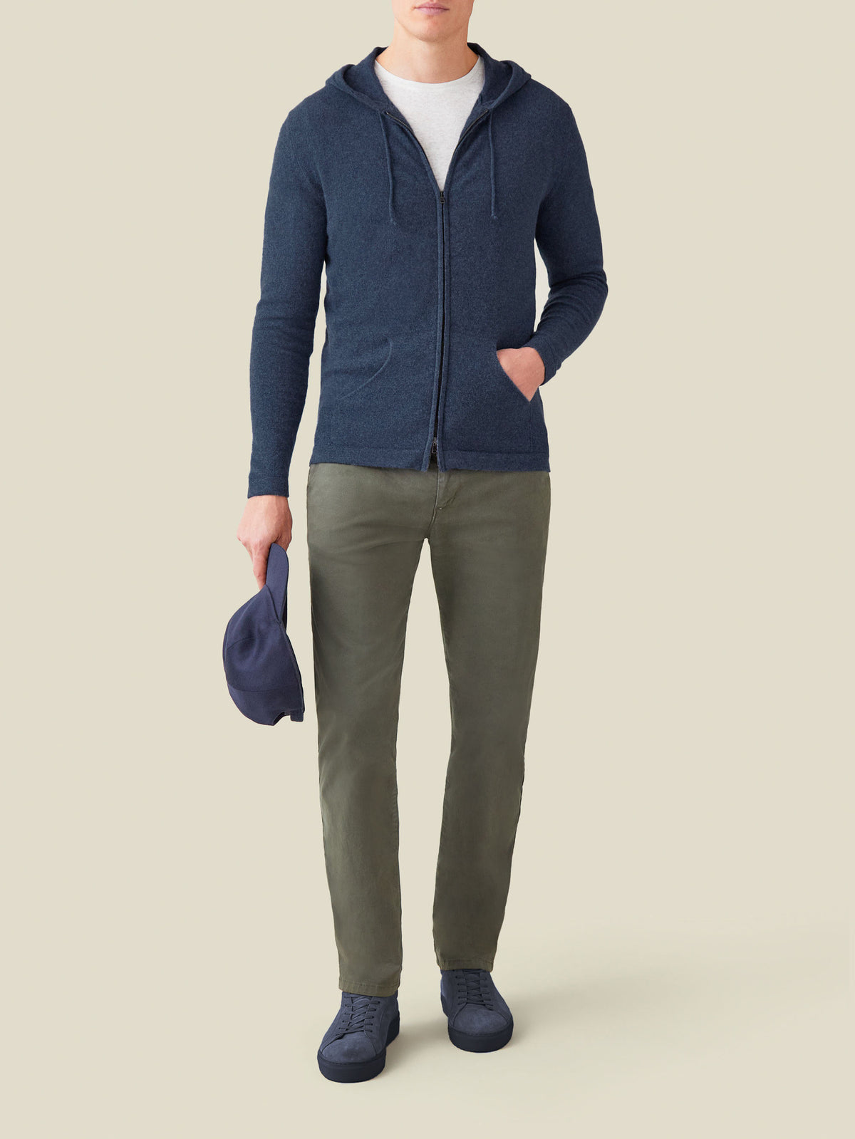Model wears the Atlantic Blue Cashmere Zip Hoodie with a white t-shirt, olive trousers and blue sneakers, holding a blue cap.