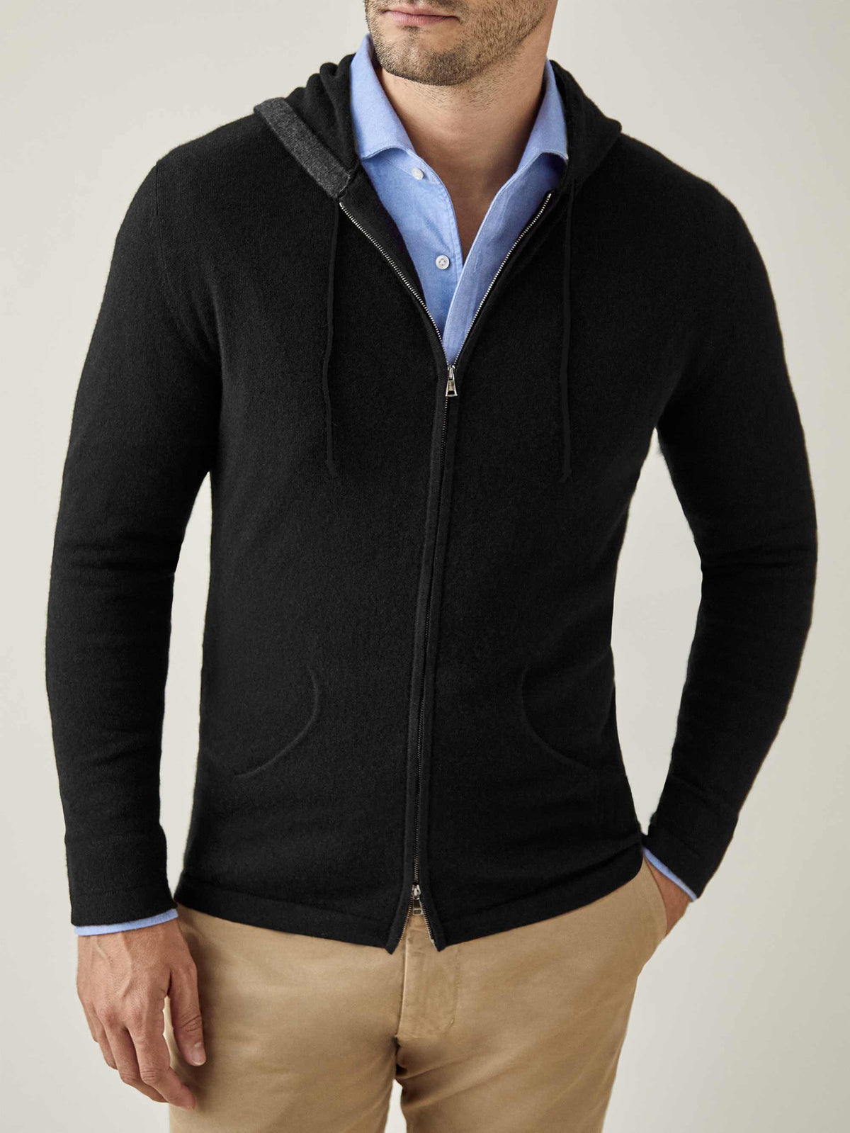 A model wears a black cashmere zip hoodie layered over a light blue collared shirt and beige chinos.