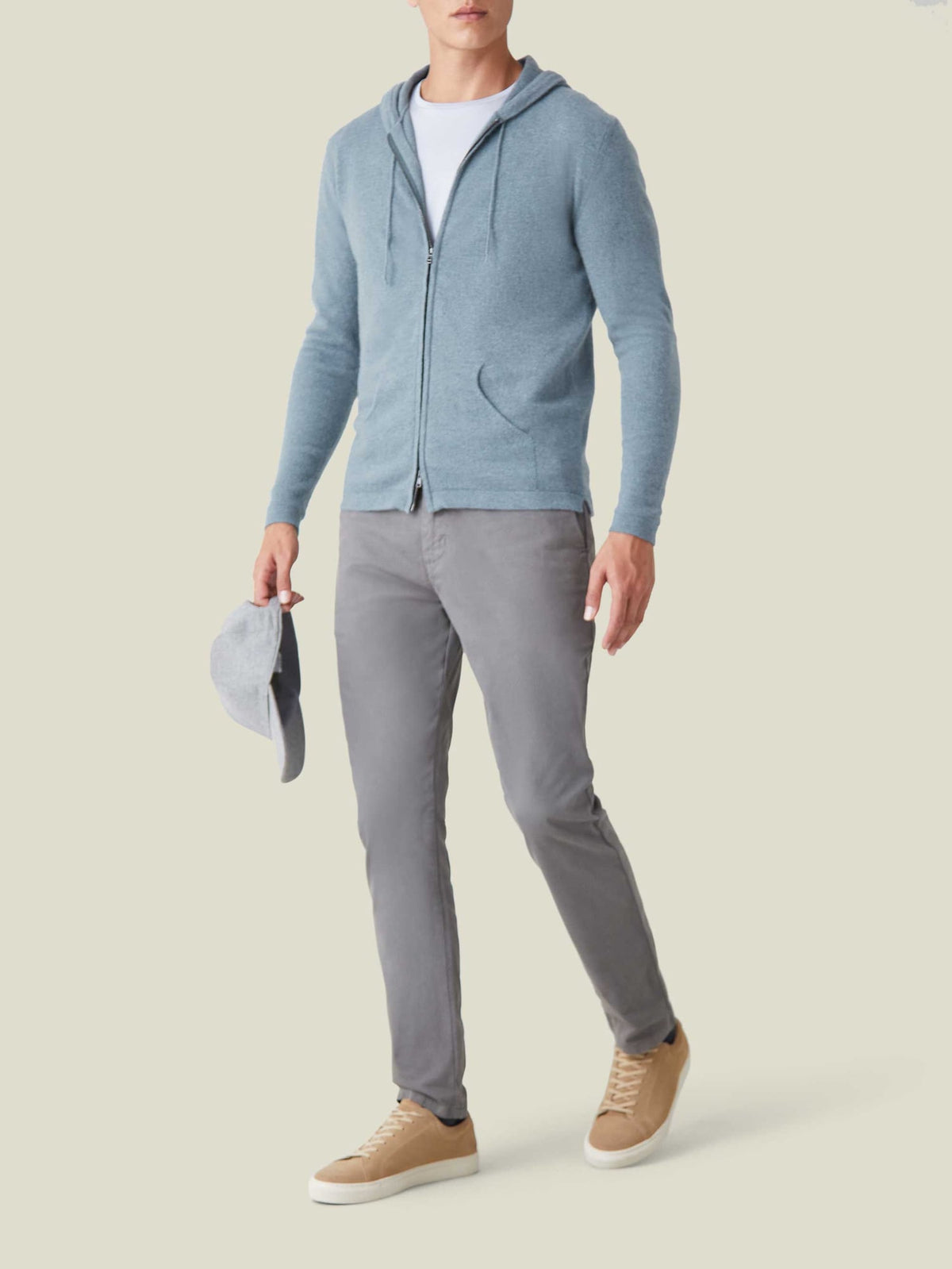 A model wears the Luca Faloni French Blue Cashmere Zip Hoodie, styled with a white t-shirt, grey trousers, and tan sneakers.