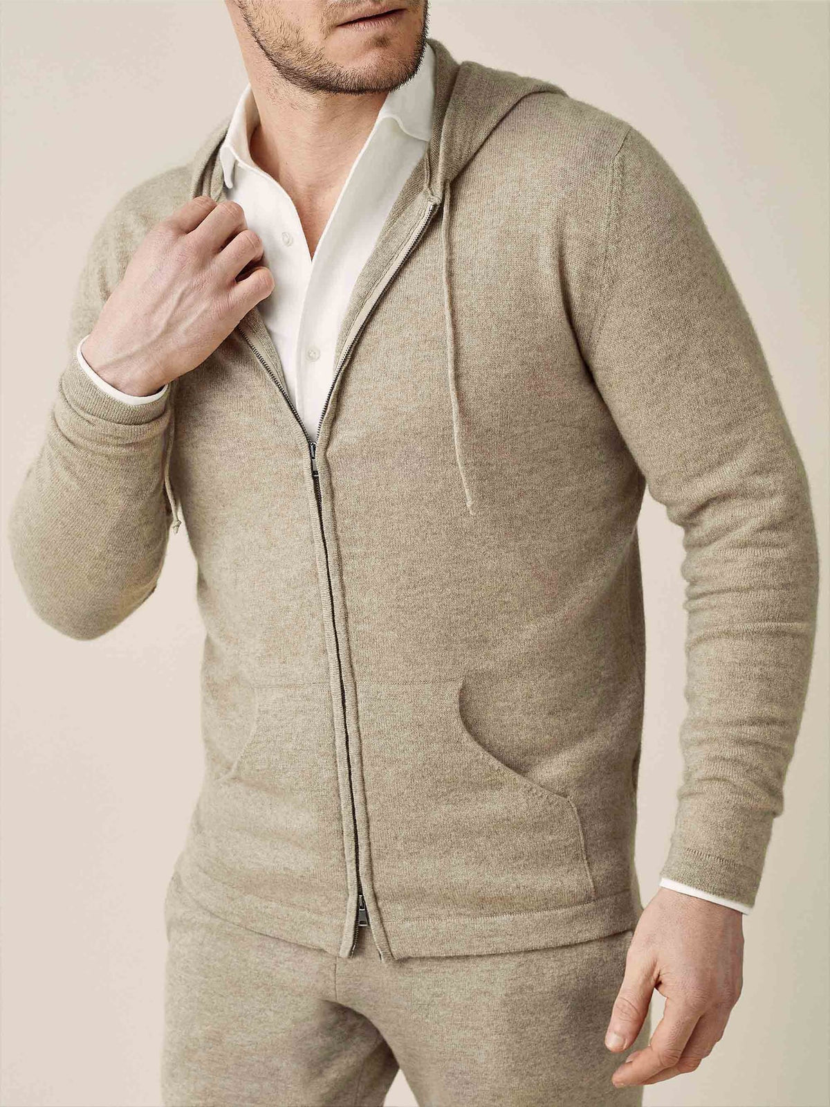A model wears the camel beige cashmere zip hoodie and matching joggers, layered over a classic white shirt.