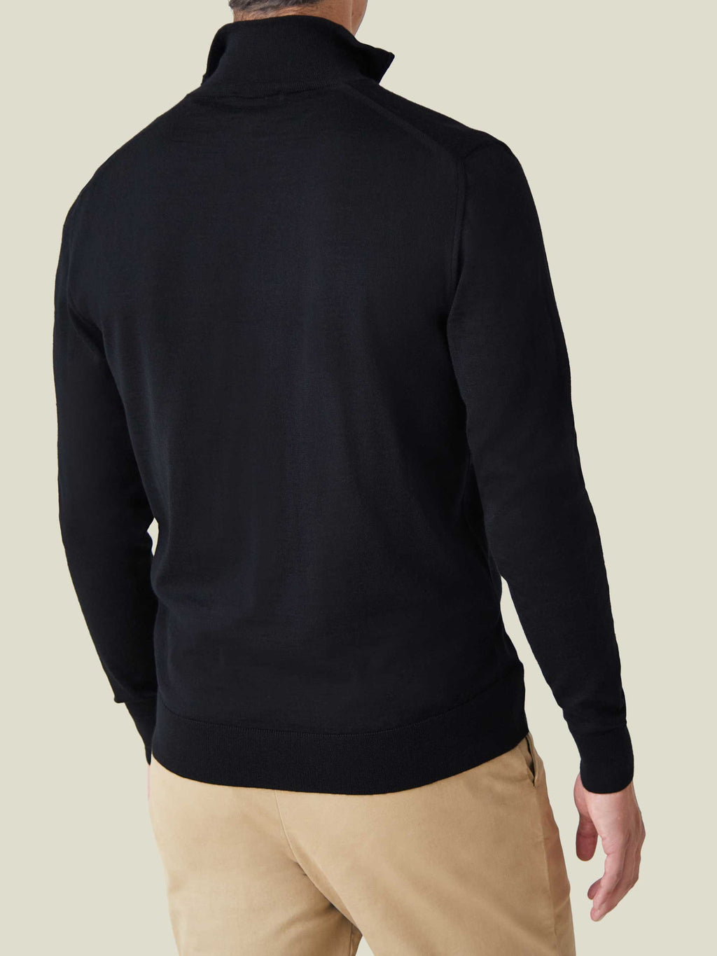 Rear view of a man wearing the black silk-cashmere quarter-zip jumper, styled with beige trousers.