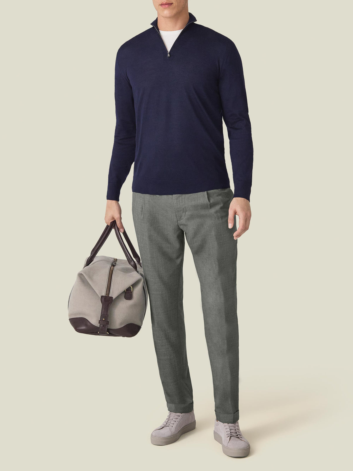 Full-length view of a man wearing the navy blue Silk-Cashmere Zip-up with grey trousers, holding a weekend bag.