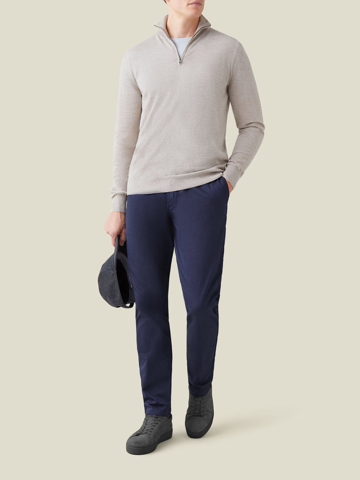 A full-length shot of a model wearing the oatmeal silk-cashmere zip-up with navy chinos and dark grey sneakers.