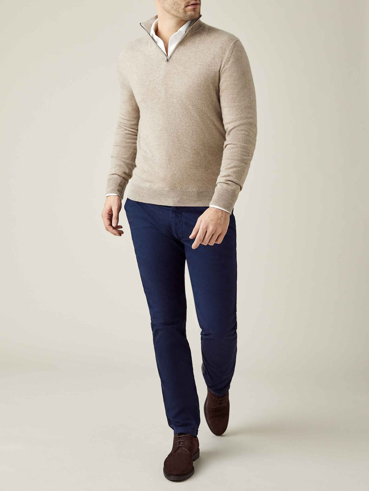 Model seen from the front wearing the camel beige cashmere zip-up sweater with a white shirt and navy trousers.