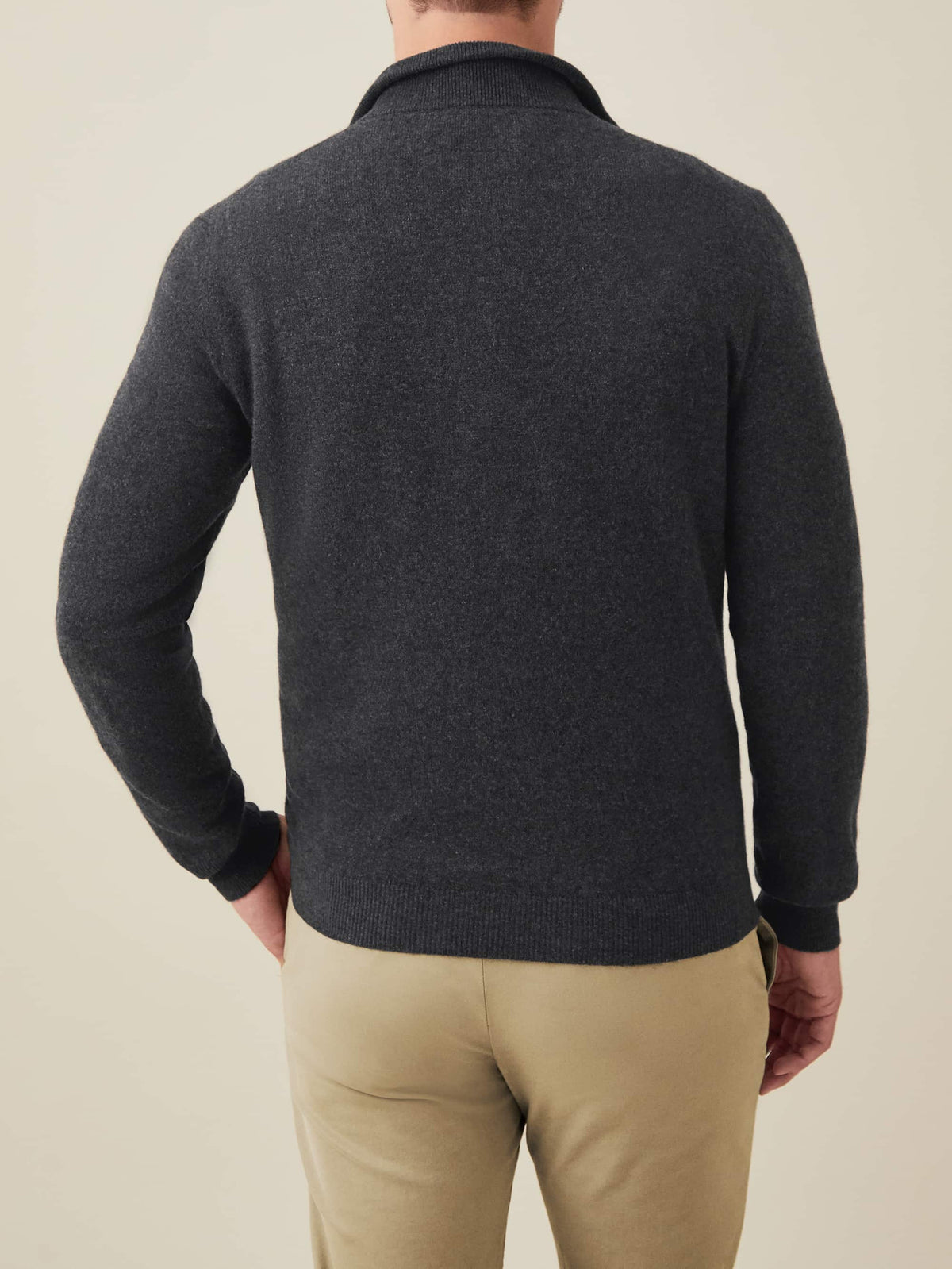 Back view of a man wearing a charcoal grey cashmere zip-up with beige chinos.