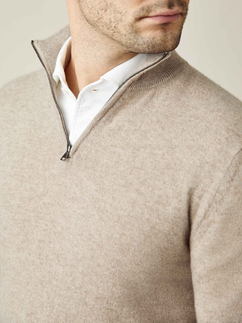 Close-up of a man wearing a camel beige cashmere zip-up over a white shirt, showing the funnel collar detail.