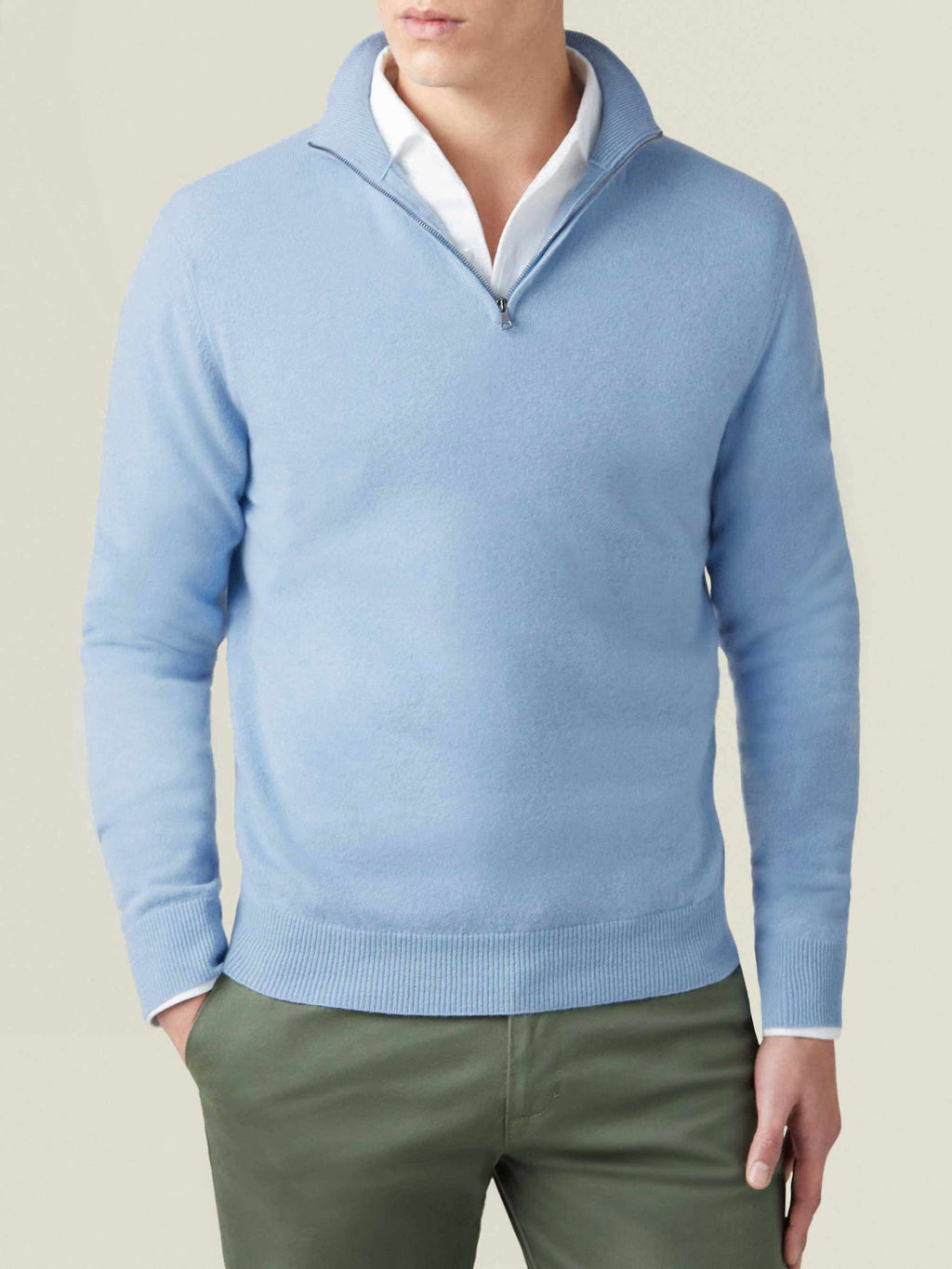 Man wears the Luca Faloni sky blue cashmere zip-up over a white shirt and green trousers.