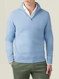 Man wears the Luca Faloni sky blue cashmere zip-up over a white shirt and green trousers.