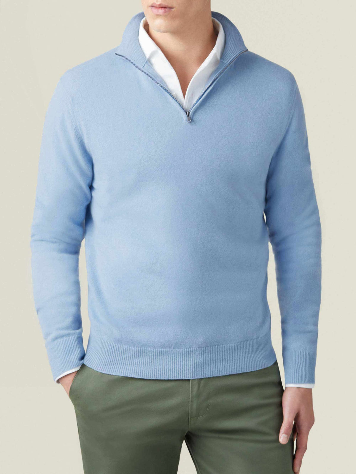 Man wears the Luca Faloni sky blue cashmere zip-up over a white shirt and green trousers.