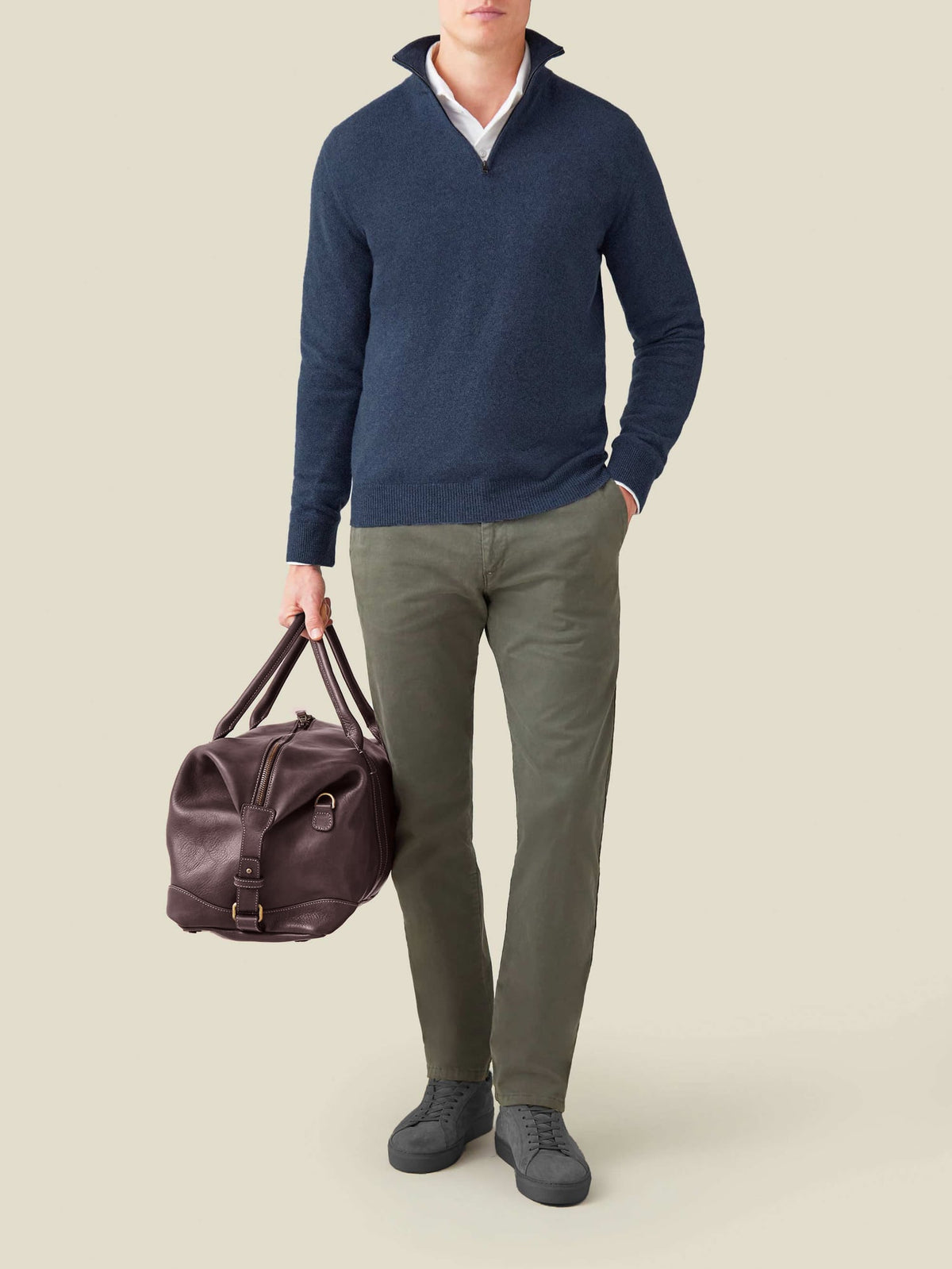 Man wearing the Atlantic Blue Cashmere Zip-up with a white shirt, green chinos, and carrying a brown leather holdall bag.