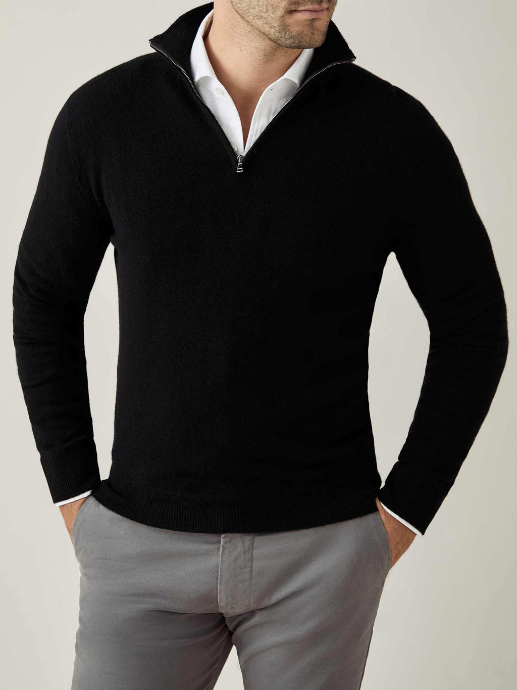 Front view of a model wearing the Black Cashmere Zip-up over a white shirt, with his hands in grey trouser pockets.