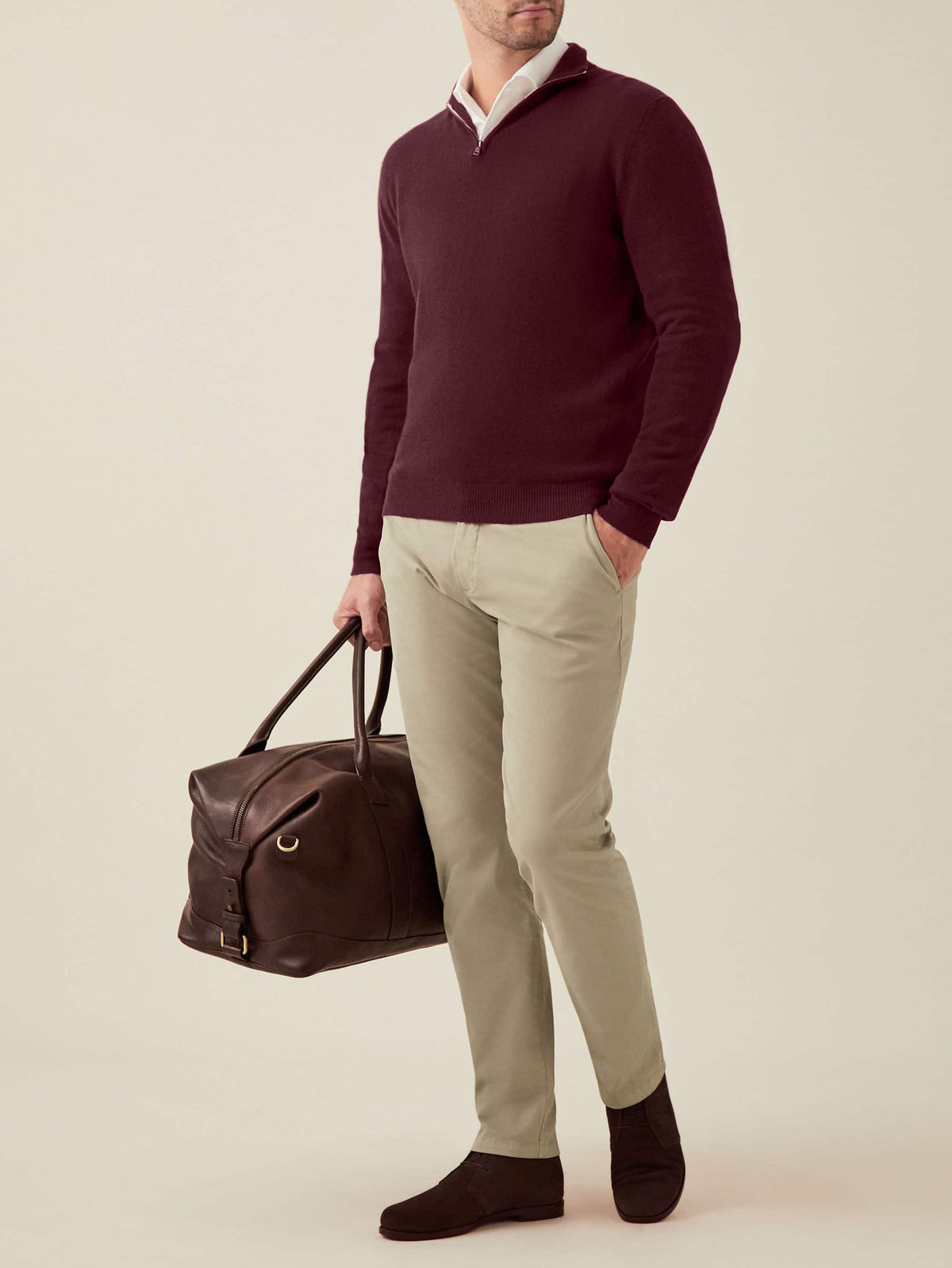 Full view of a model wearing the Luca Faloni Grape Cashmere Zip-up with beige chinos and holding a brown leather travel bag.
