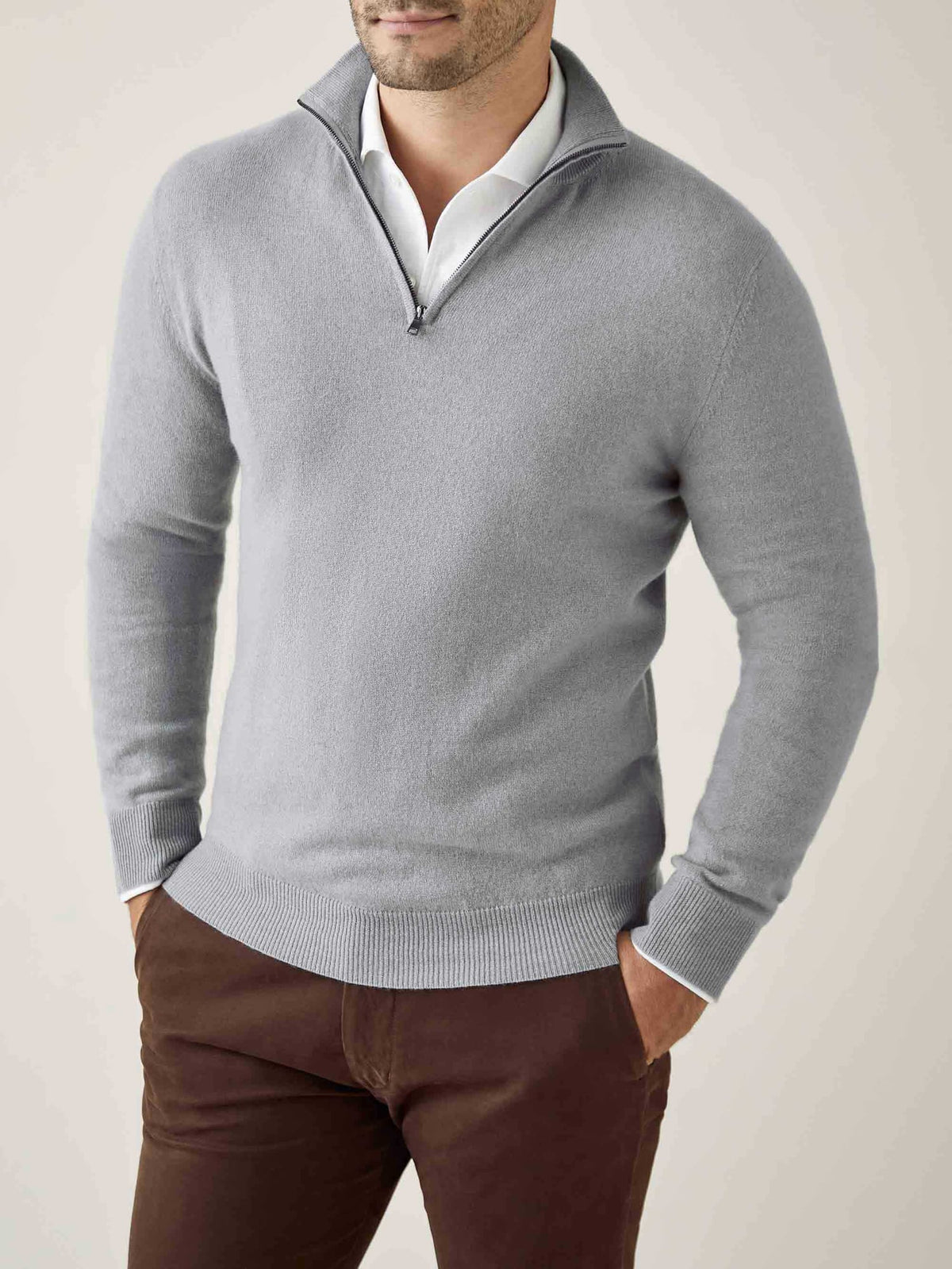 Man wearing a misty grey cashmere zip-up over a white shirt and brown trousers, shown from the front.