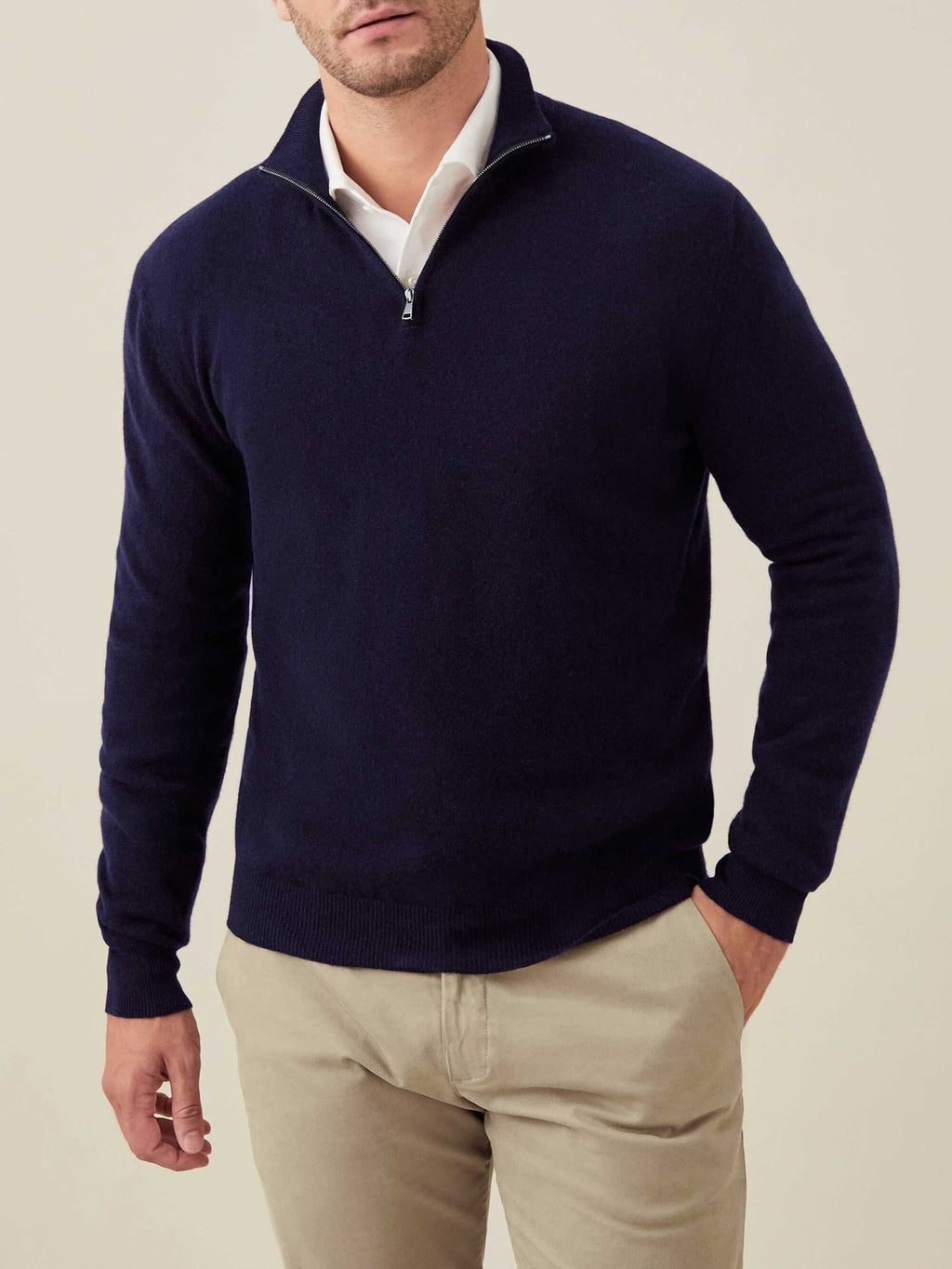 A man wears the Luca Faloni Cashmere Zip-up in Midnight Blue over a white collared shirt and beige trousers.
