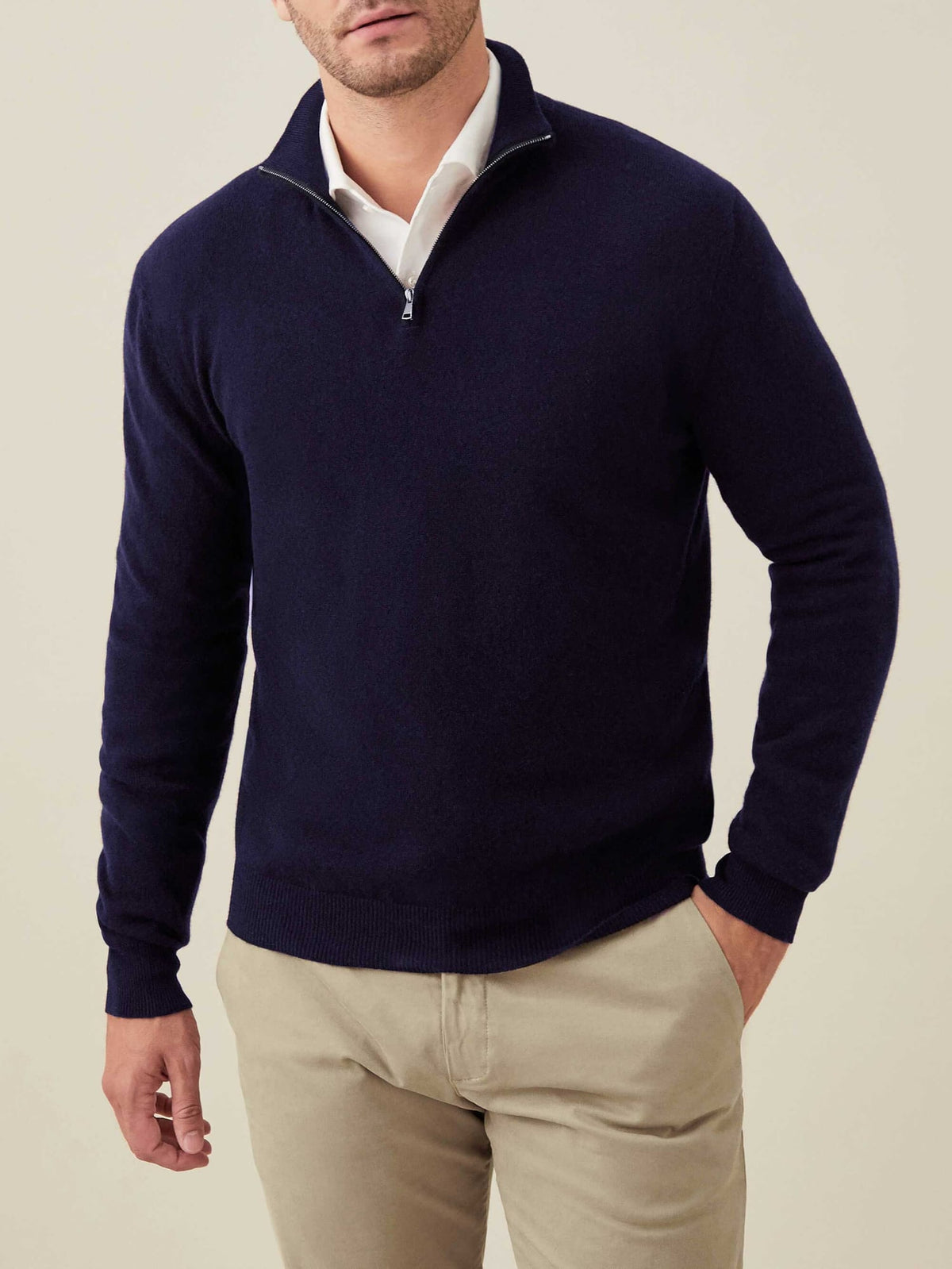A man wears the Luca Faloni Cashmere Zip-up in Midnight Blue over a white collared shirt and beige trousers.