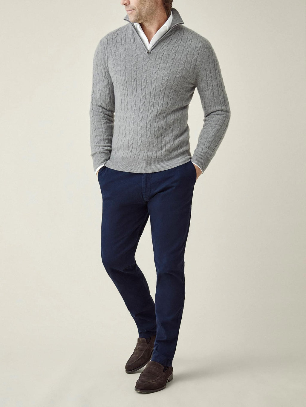 A full-length shot of a man wearing the Dolomiti Grey Cable Knit Zip-up with navy trousers and brown suede loafers.