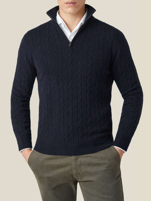Front view of a model wearing a midnight blue cashmere cable knit zip-up sweater over a white shirt and olive trousers.