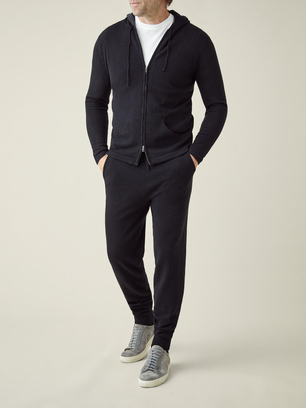 Front view of a model in Luca Faloni's black cashmere joggers, paired with the matching zip hoodie and grey suede sneakers.