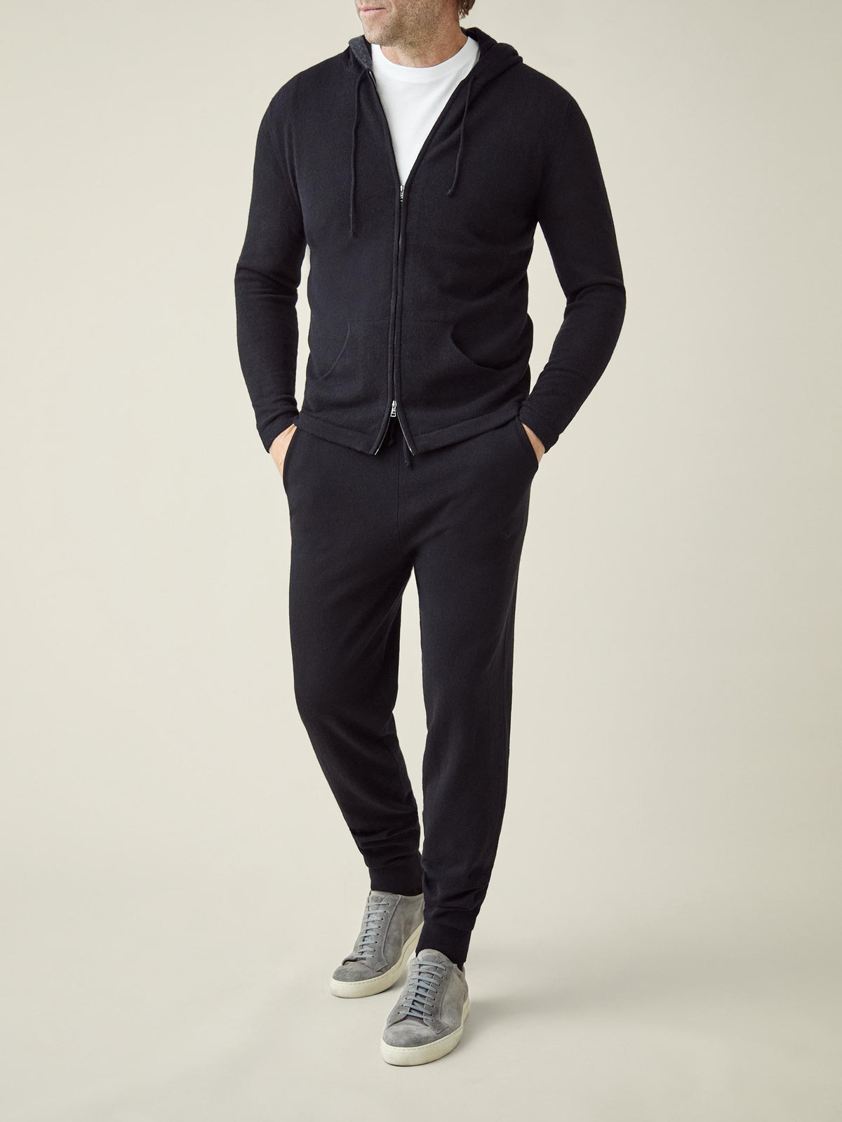 Front view of a model in Luca Faloni's black cashmere joggers, paired with the matching zip hoodie and grey suede sneakers.