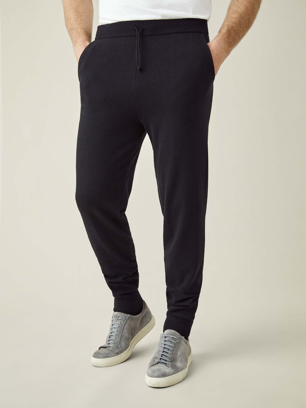 A front view of a model wearing Luca Faloni's tapered fit Black Cashmere Joggers with grey suede trainers.