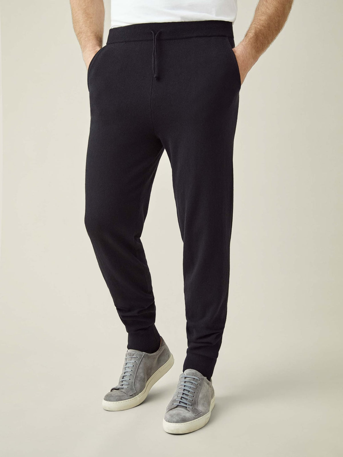 A front view of a model wearing Luca Faloni's tapered fit Black Cashmere Joggers with grey suede trainers.
