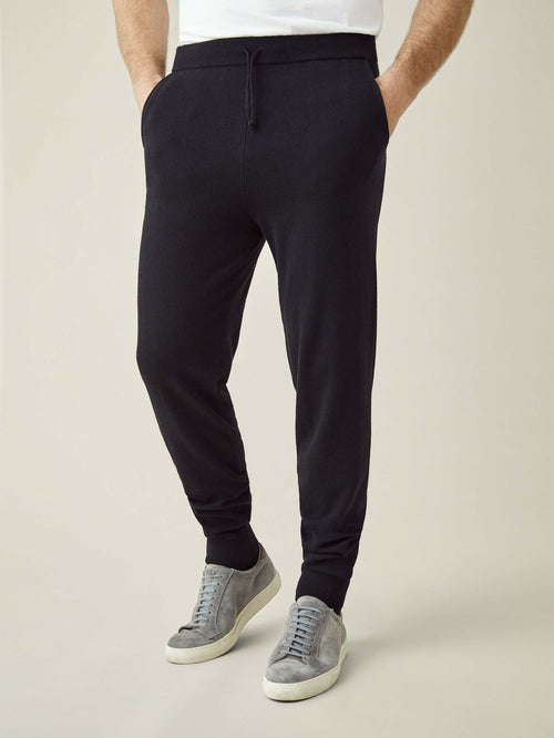 A front view of a model wearing Luca Faloni's tapered fit Black Cashmere Joggers with grey suede trainers.