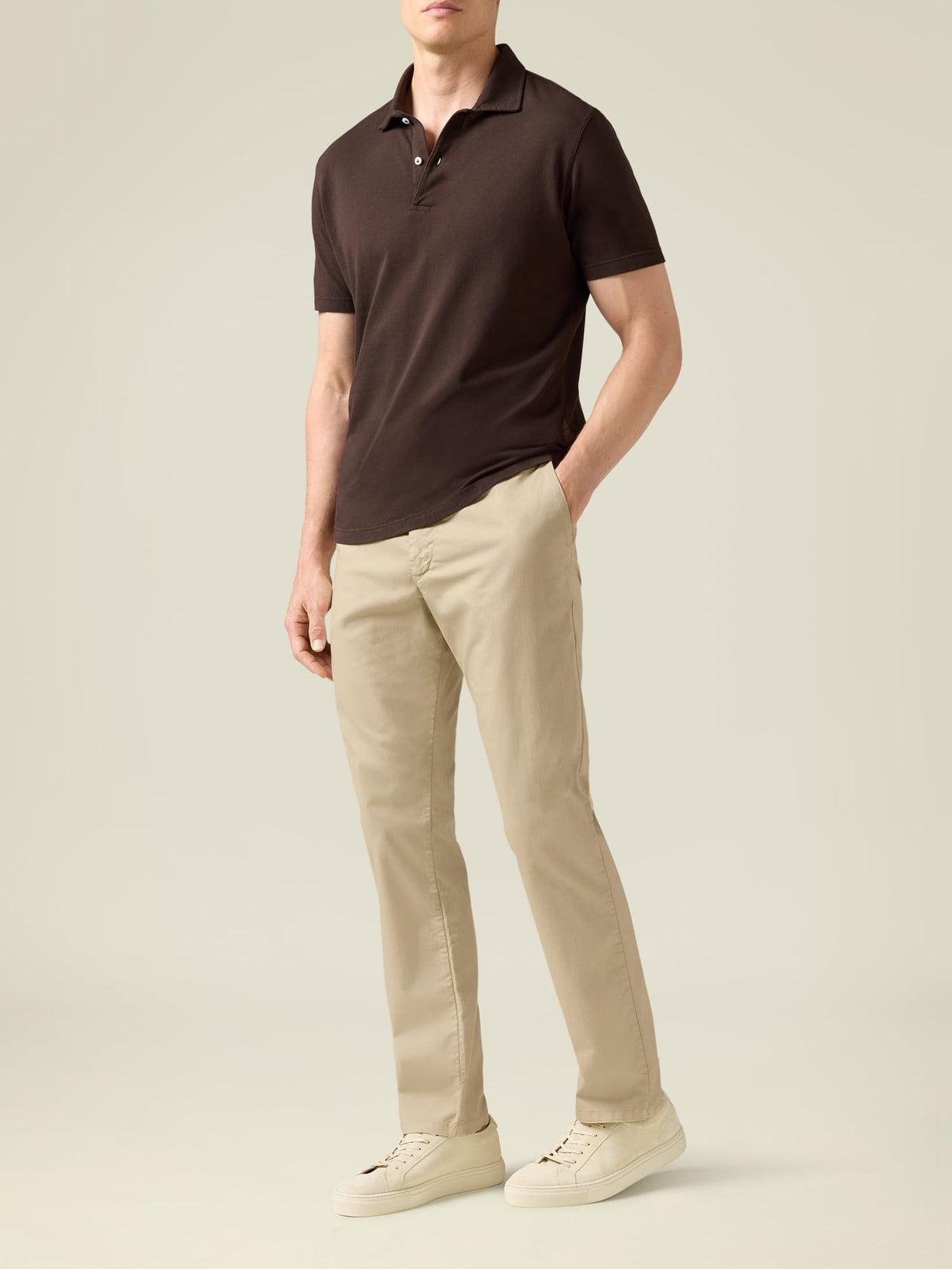 A model wears the Luca Faloni Classic Piqué Polo in Chocolate Brown, paired with beige chinos and cream trainers.